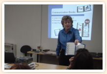A woman in front of a presentation screen, showing a communication book